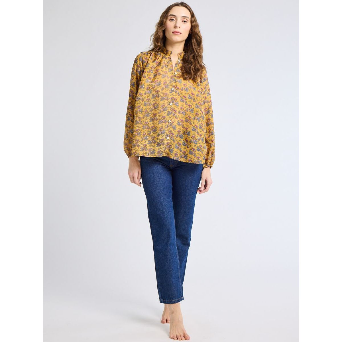 Woman wearing a yellow floral blouse and blue jeans on a white background