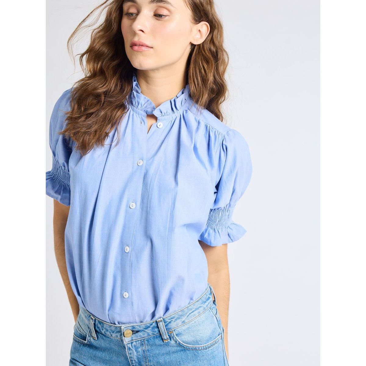 Woman wearing a light blue blouse with ruffled sleeves on a white background