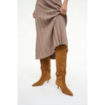 Brown knee-high boots worn with a pleated skirt on a white background