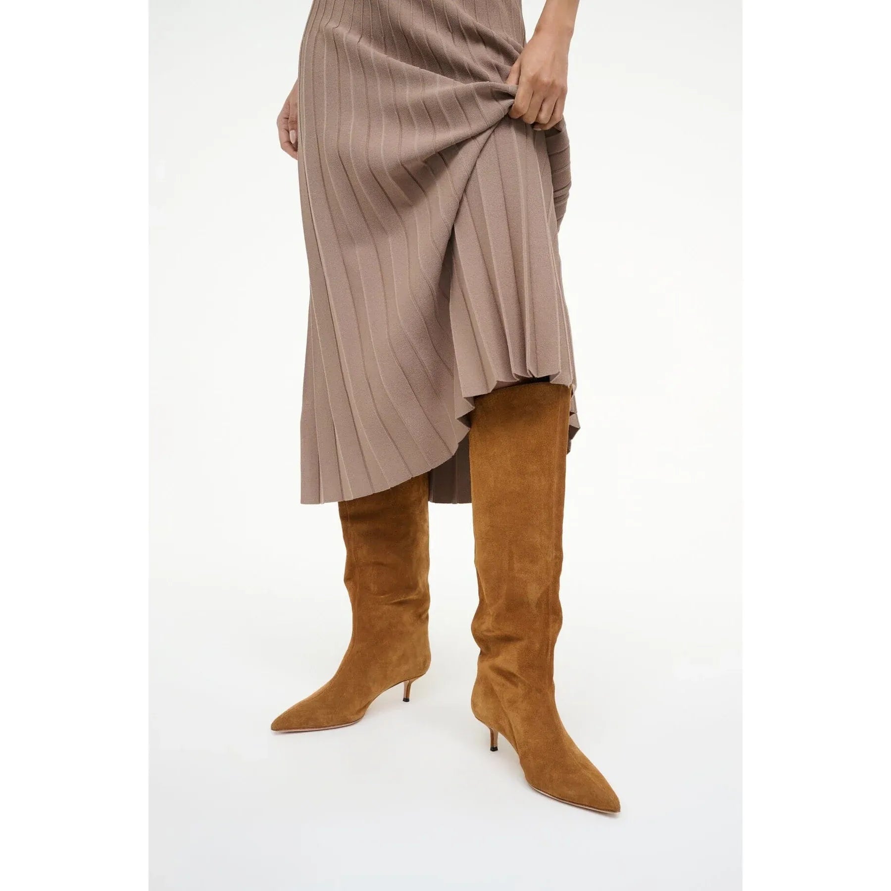 Brown knee-high boots worn with a pleated skirt on a white background