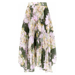 The Christy Lynn Gwen Skirt - Midnight Garden by Christy Lynn is a flowy, pleated skirt featuring a floral pattern in shades of pink, yellow, and green on a dark green background. Its asymmetric hem offers a lightweight and elegant appearance, making it perfect for any occasion.