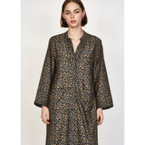 A person with shoulder-length hair is wearing a long-sleeved, patterned Mirth Malmo Dress in Navy Lilypad, made in India. The hand screen-printed design features an intricate, repeating pattern in a mix of brown and dark colors. They are standing against a plain background.