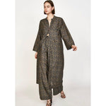 A model wearing the Mirth Malmo Dress in Navy Lilypad, featuring a long, patterned open-front coat and wide-leg trousers. The fabric, hand screen printed and Made in India, showcases a detailed blue and brown geometric design. The model is posing against a plain white background, accessorized with dark strappy sandals.