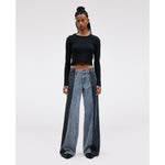 A person with long braided hair stands confidently, wearing the SLVRLAKE RE-Work Mica Panel Lunar Eclipse black long-sleeve crop top along with high-rise cropped wide-leg blue jeans. The neutral background highlights their crafted outfit and posture.