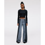 A person with long braided hair stands confidently, wearing the SLVRLAKE RE-Work Mica Panel Lunar Eclipse black long-sleeve crop top along with high-rise cropped wide-leg blue jeans. The neutral background highlights their crafted outfit and posture.