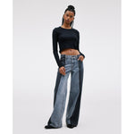 A person with long braided hair stands confidently in the SLVRLAKE RE-Work Mica Panel Lunar Eclipse, featuring a black long-sleeve crop top and high-rise, cropped wide-leg jeans. Their left hand is casually placed in a pocket, posing against a plain light background.