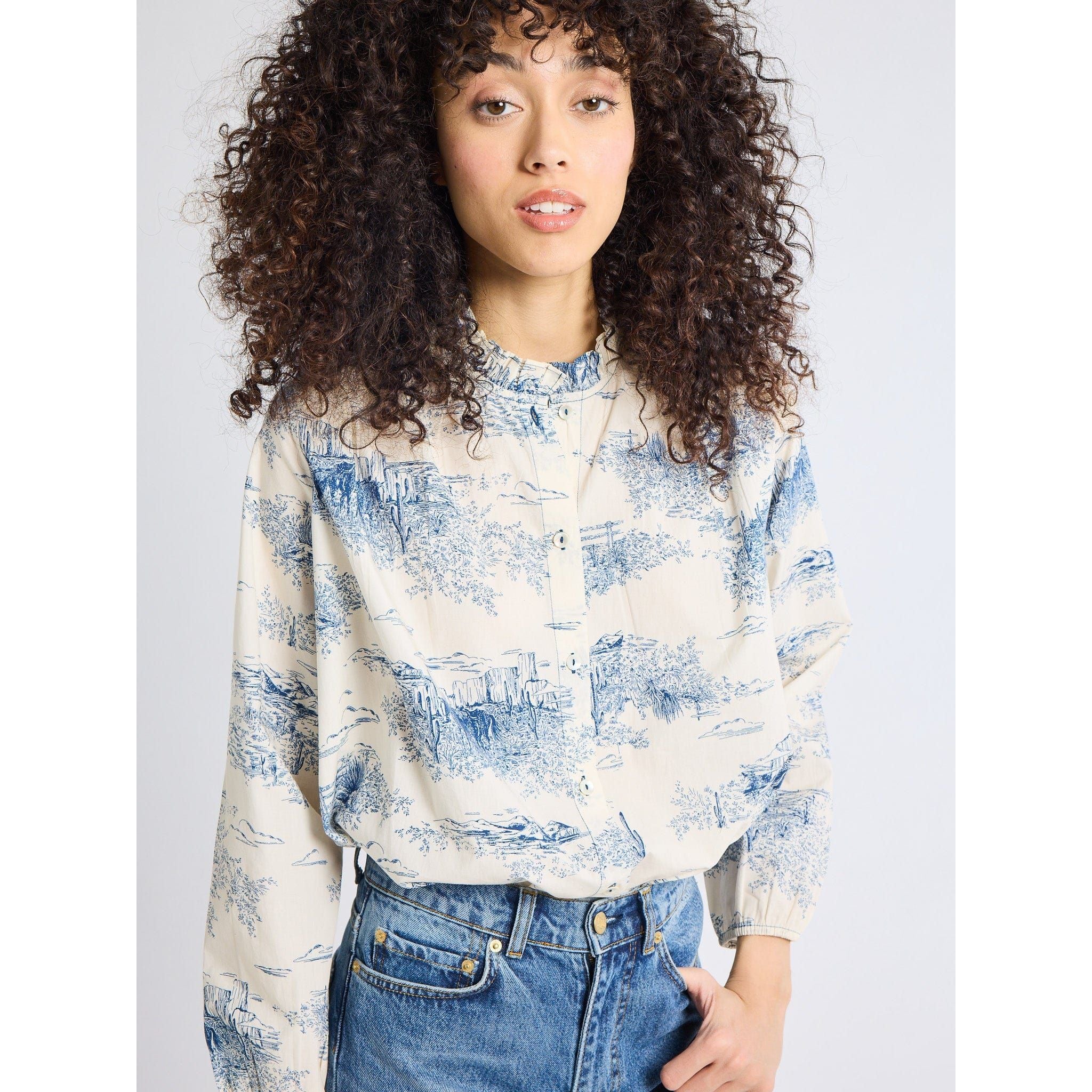 Woman wearing a blue and white patterned blouse with jeans on a plain background