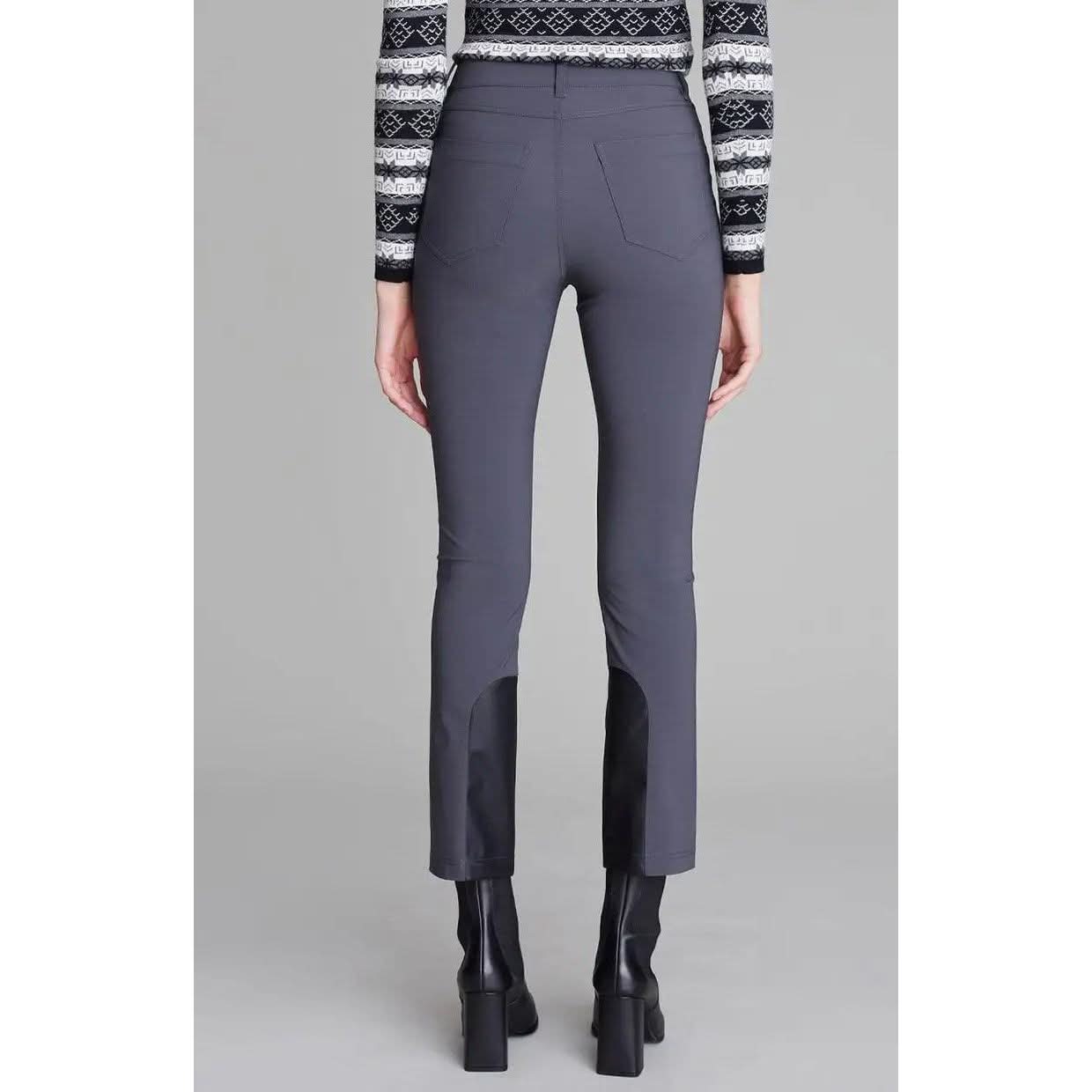 A person is standing facing away, wearing the Alp N Rock Naomi Straight Leg Pant in Charcoal, which features black patches on the lower legs and a slim straight-leg silhouette for a sleek touch. They are also sporting black high-heeled boots and a long-sleeved, black and white patterned sweater. The background is plain gray.