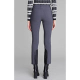 A person is standing facing away, wearing the Alp N Rock Naomi Straight Leg Pant in Charcoal, which features black patches on the lower legs and a slim straight-leg silhouette for a sleek touch. They are also sporting black high-heeled boots and a long-sleeved, black and white patterned sweater. The background is plain gray.
